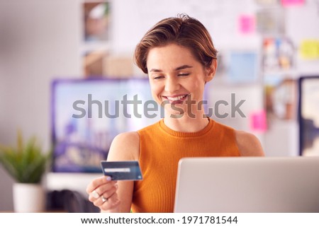 Female Architect In Office Working At Desk Making Online Purchase Using Credit Card On Laptop