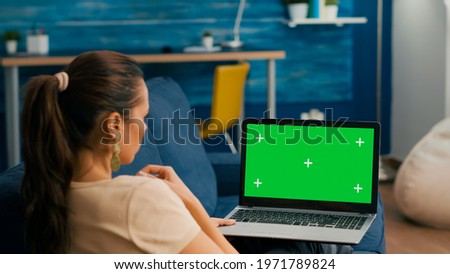 Freelancer sitting on couch working on business ideas using laptop computer with mock up green screen chroma key display. Caucasian female searching the network use isolated pc