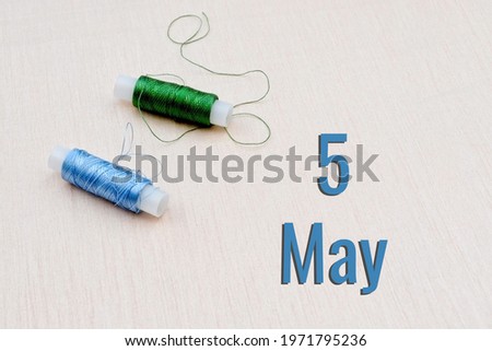 Handicraft calendar 5 may. Skeins of green and blue threads for embroidery on beige background. Handmade concept.
