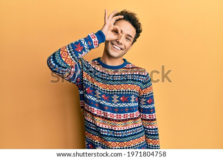 Young handsome man wearing casual winter sweater smiling happy doing ok sign with hand on eye looking through fingers 