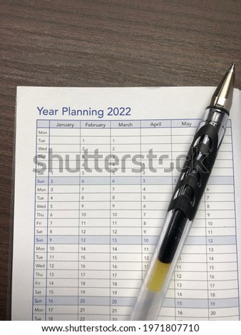 Selective focus of book with Year planning 2022 inscription with month and pen on wooden background. Business, planning, employees, decision during coronavirus and Covid-19.