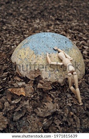 Wooden dummy lay down sadly on a round stone against the backdrop of withered foliage. Earth and ecology problems