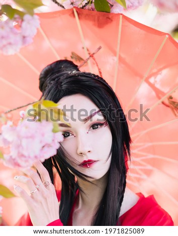 Portrait of young woman in image of geisha near blooming sakura dressed japanese traditional kimono with umbrella in her hand.