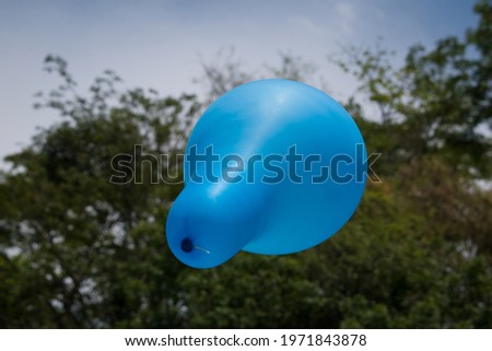 Closeup picture of sky blue balloon flying and blue sky and green trees in background.