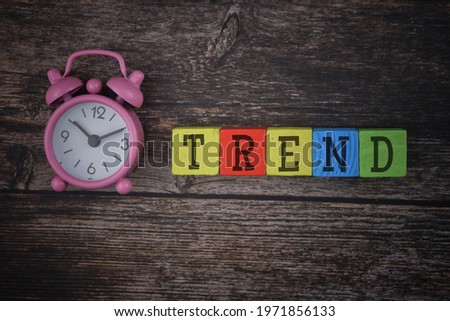 Trend wording on a wooden block with clock over a wooden background.
