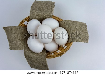 White chicken eggs lie in a wooden basket on a textured napkin, white background