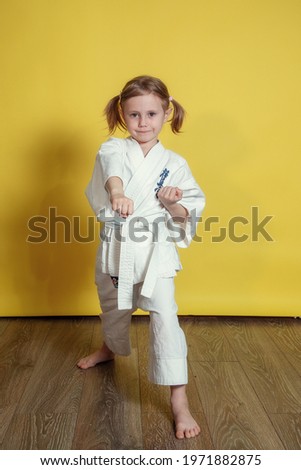 Portrait Of 5 year old caucasian Girl in kimono Practicing Karate Against yellow Background at home