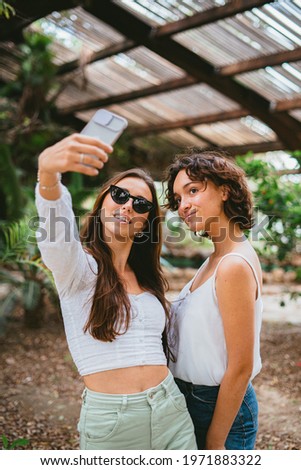 Two young teen girls taking a selfie to share it on social media. They are having fun at the park.
