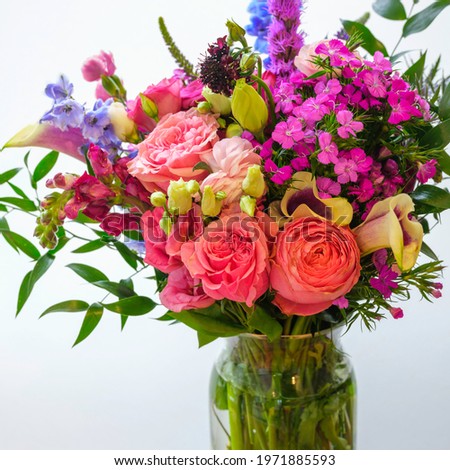 Spring flowers bouquet in a glass vase. Warm tone pink roses, carnations, and wildflowers. Fresh uplifting flora on white background.