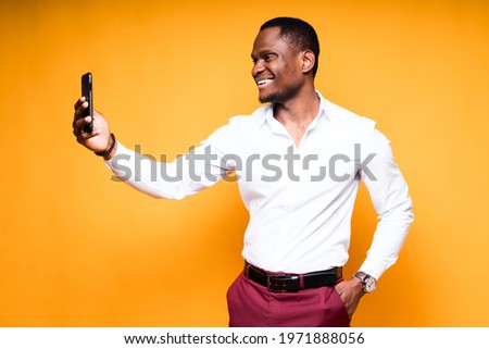 Happy dark-skinned man in shirt holding phone in hand and taking selfie smiling
