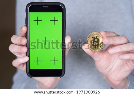 Cropped image of woman's hand showing green screen on smart phone and golden bitcoin coin