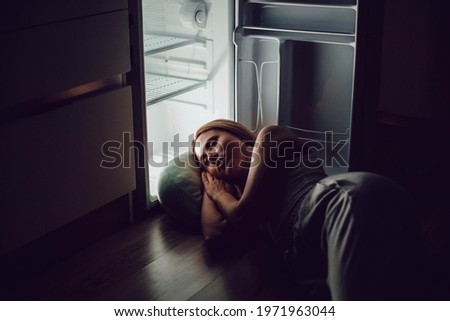 A young woman is sleeping by the open refrigerator. The girl escapes from the heat without air conditioning. Royalty-Free Stock Photo #1971963044