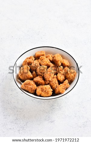 Crispy fried breaded chicken bites in bowl over light stone background with copy space. Tasty chicken nuggets. 