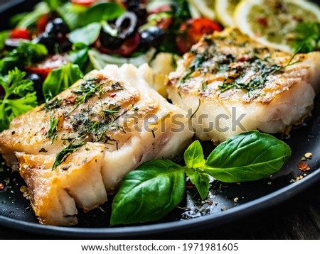 Fish dish - fried cod fillet with fresh vegetable salad on wooden table 
