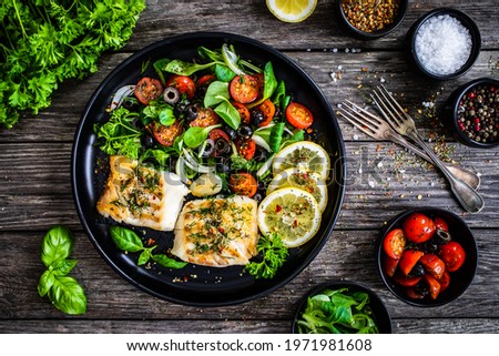 Fish dish - fried cod fillet with fresh vegetable salad on wooden table  Royalty-Free Stock Photo #1971981608