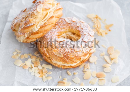 French traditional cake Paris Brest with praline cream, powdered sugar and almond petals on top on a gray concrete background. Copy space