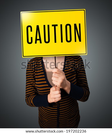 Young lady standing and holding a yellow caution sign in front of her head