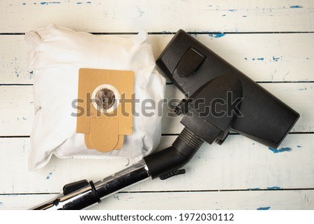 Used full dust bag of a vacuum cleaner with a black plastic vacuum cleaner brush are lying on the white with blue spots painted wooden boards Royalty-Free Stock Photo #1972030112