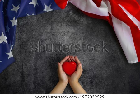 American Flag next to child's hands holding red heart- symbol of gratitude and love for Memorial Day or 4th of July. Flag Day.Greeting card or banner for website or store sale. copy space. Layout