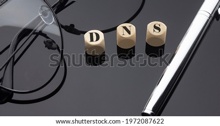 DNS concept, words on wooden blocks on black background with pen and glasses.