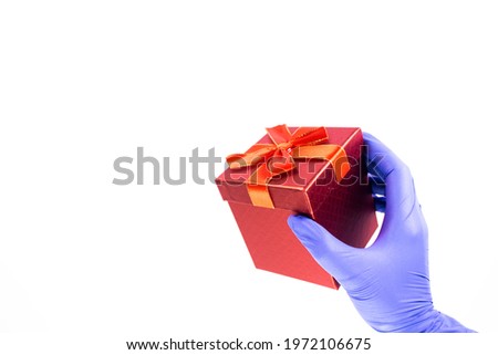 Women's hand in medical gloves hold a gift box with a red ribbon on a white background. Concept of sales and gifts during Coronavirus. Quarantine. Delivery courier. Online purchase