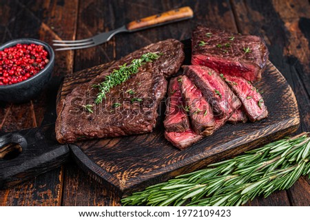 Grilled sliced skirt beef meat steak on a cutting board with herbs. Dark wooden background. Top view Royalty-Free Stock Photo #1972109423