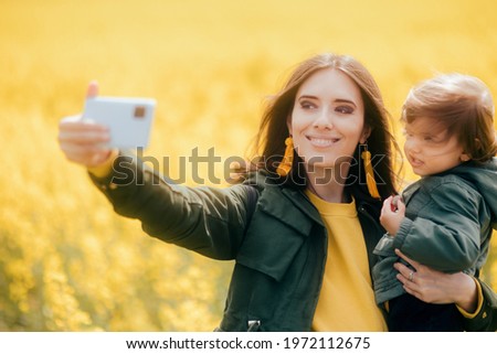 Happy Mom and Daughter Taking Selfies in Rapeseed Field. Mother taking mobile photos with her little girl outdoors in nature during family vacation trip
