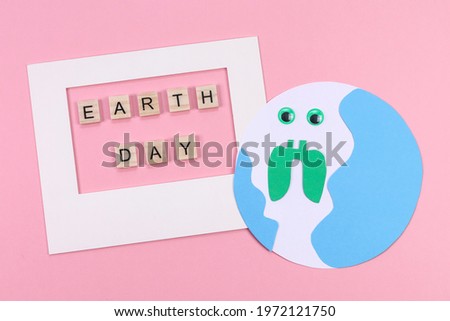 Creative planet and white paper frame with the inscription from wooden cubes: earth day lie on a pink background, top view close-up.