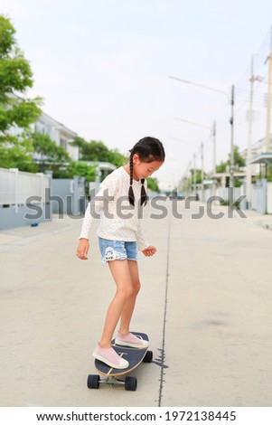 Asian little girl child skating on a skateboard. Kid riding on skateboard outdoors at the street. She skateboarding on the road