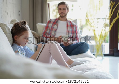 Happy father smilling daughter sitting on sofa enjoying creative activity, drawing pen pictures in albums, father and daughter spend free time together