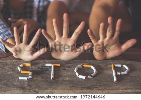 The word stop spelled using cigarettes on wooden background with stop hands