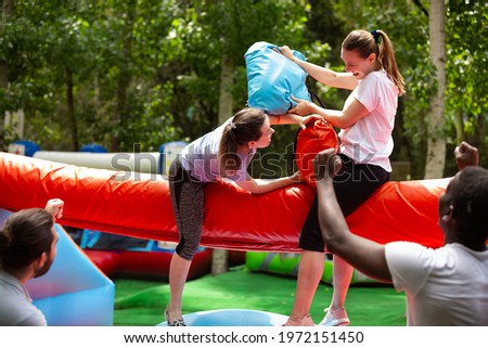 Cheerful girlfriends fighting with inflatable pillows in an amusement park