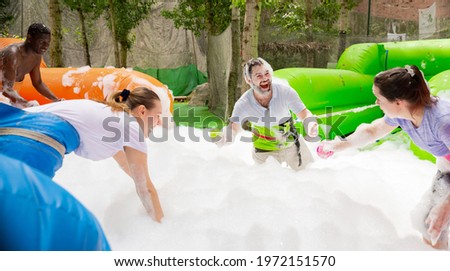 Game of funny friends in soap suds on an inflatable trampoline