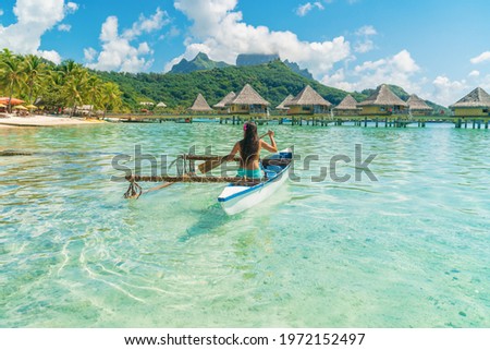 French Polynesia Tahiti travel vacation concept. Outrigger Canoe polynesian watersport sport woman paddling in traditional vaa boat. Water leisure activity, Bora Bora overwater bungalow resort hotel. Royalty-Free Stock Photo #1972152497