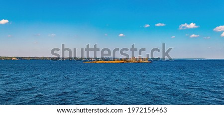 Small island on the sea horizon against the background of the sky. Water surface. Seascape. Rivers and lakes. Dnepr River. Coastline. Cloudy horizon. Panoramic photo. Blue sky.