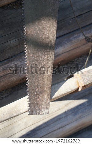 Tool for sawing wood planks - hand saw. Iron base, covered with irrosion in places, black handle. Vitit on a carnation with a wire on the wall from an old wooden bar.