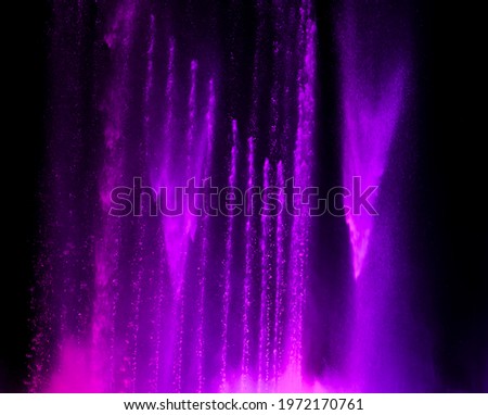 Splashing fountain in purple color at night as background.