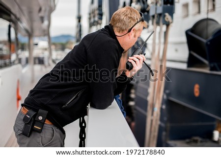 Superyacht crew member coordinating a vessel haul out on travel lift with handheld radio Royalty-Free Stock Photo #1972178840