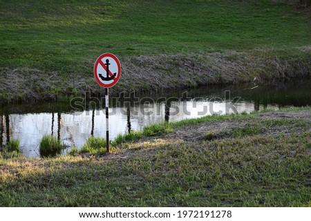 Sign prohibiting anchoring in a gutter. A narrow river between the high banks.