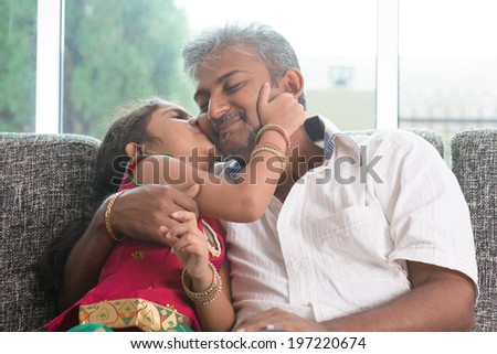 Happy Indian family at home. Asian sweet daughter kissing her father face indoor, sitting on sofa.