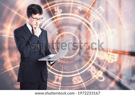 Businessman holding a laptop and thinking in an office corridor with a circle with zodiac signs, prediction and astrology concept