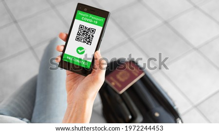 Digital Health Passport app for smartphone with vaccinated sign and quad code. Woman leaving with passport and baggage. Coronavirus concept. Royalty-Free Stock Photo #1972244453
