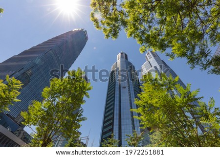 Looking up at the tall buildings in Beijing's central business district, the sun shines on the trees. Modern office building background concept. Beijing, China.