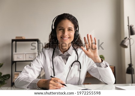 Telehealth. Headshot portrait of smiling latin woman doctor physician wear headphones look at camera wave hand to spectators. Young female medic consult remotely at virtual online meeting with patient Royalty-Free Stock Photo #1972255598