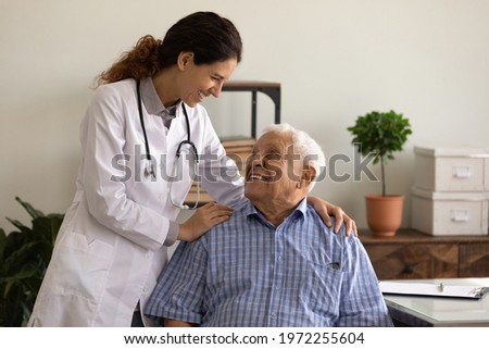 Laughter is the best medicine. Optimistic young lady doc embrace shoulders of laughing old man sitting on chair at clinic office. Doctor joking with aged patient give support motivation on good result Royalty-Free Stock Photo #1972255604