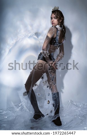 Model in black boots and long transparent dress with seashells. Crown of seashells on head. Creative illumination with glare on the wall