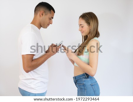 Young man and woman in casual wear standing and holding mobile phone isolated over white background