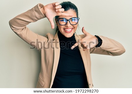 Young hispanic woman wearing business style and glasses smiling making frame with hands and fingers with happy face. creativity and photography concept. 