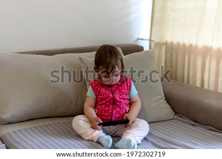 Little Caucasian girl using smartphone. Little cute toddler girl plays with a mobile phone. Child is watching her favorite cartoon on the internet over the phone. People and technology concept.