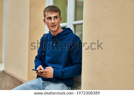 Young blond student smiling happy using smartphone at the university.